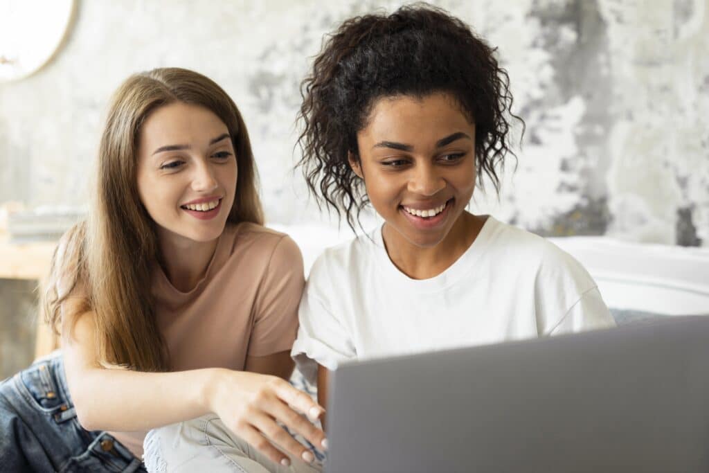 two smiley friends looking laptop together 1 - - Derniers secours